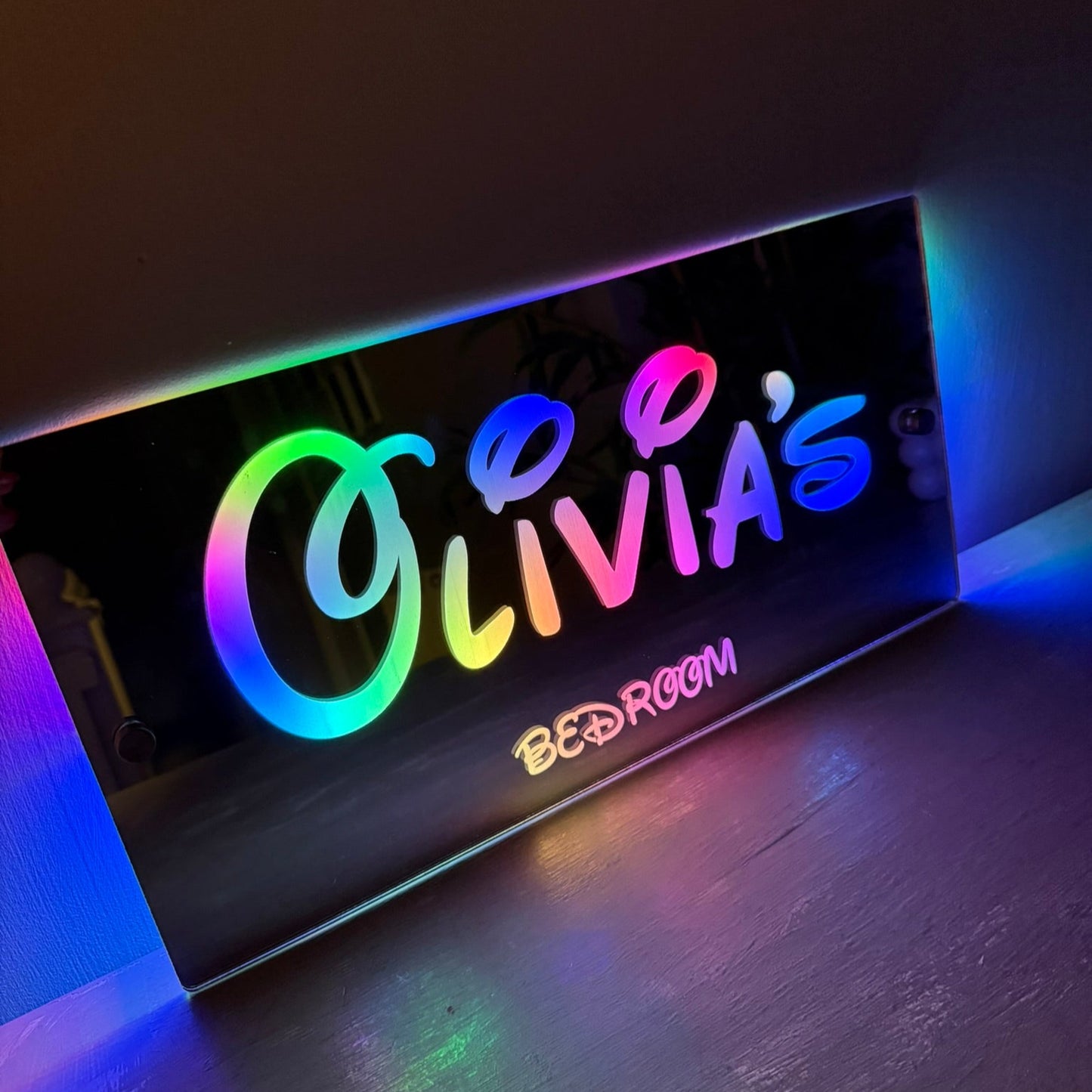 Personalised LED mirror bedroom sign with Disney-style font lit in colourful lights, perfect for kids’ rooms.