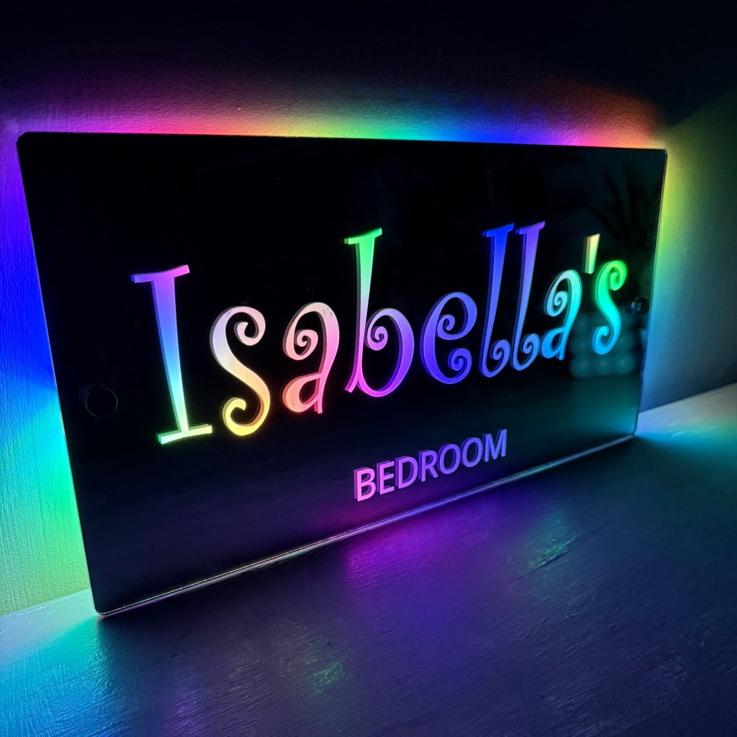 Personalised LED mirror bedroom sign with custom swirly font glowing in soft pastel lights, perfect for a girl's room.