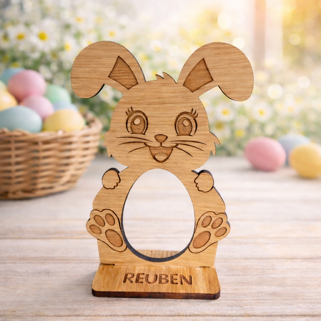 Wooden rabbit-shaped photo frame with 'REUBEN' engraving on a wooden surface with Easter eggs in the background.