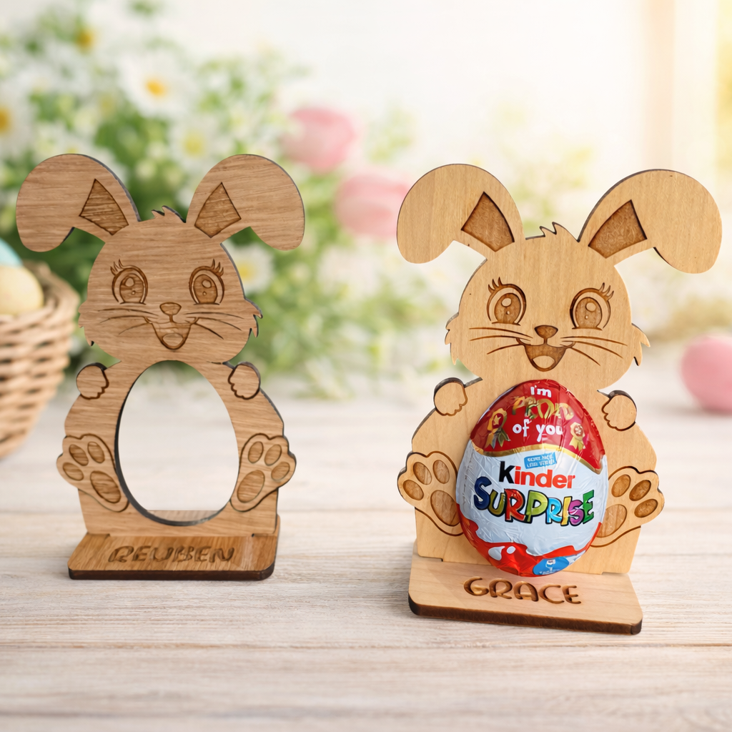 Wooden rabbit-shaped holders with Kinder Surprise eggs on a wooden surface with blurred Easter decorations in the background.