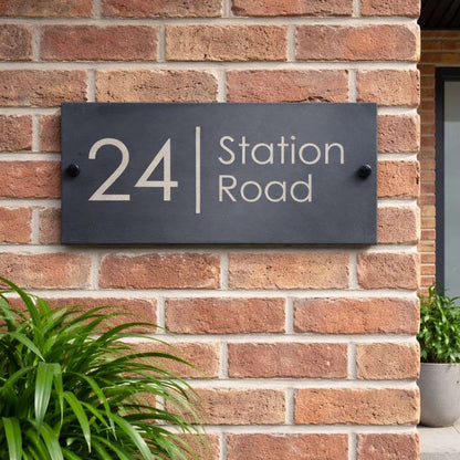 House number sign '24 Station Road' on a brick wall with plants.