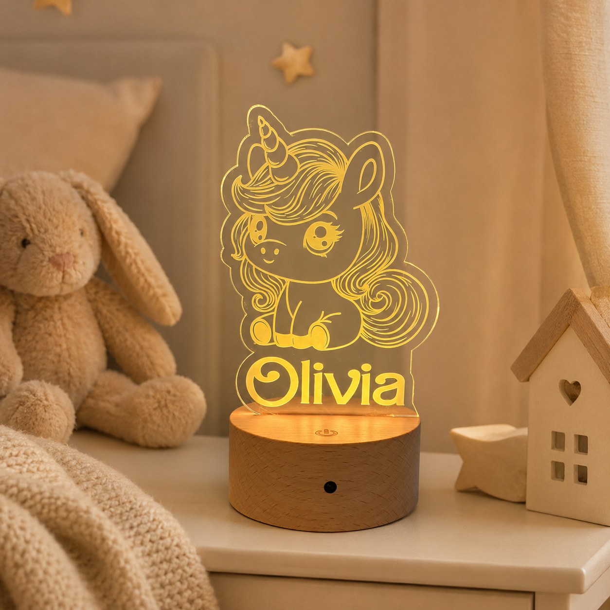 A personalized LED night light shaped like a cartoon unicorn with the name 'Olivia' on the base, placed on a bedside table in a cozy bedroom setting with a stuffed bunny nearby.