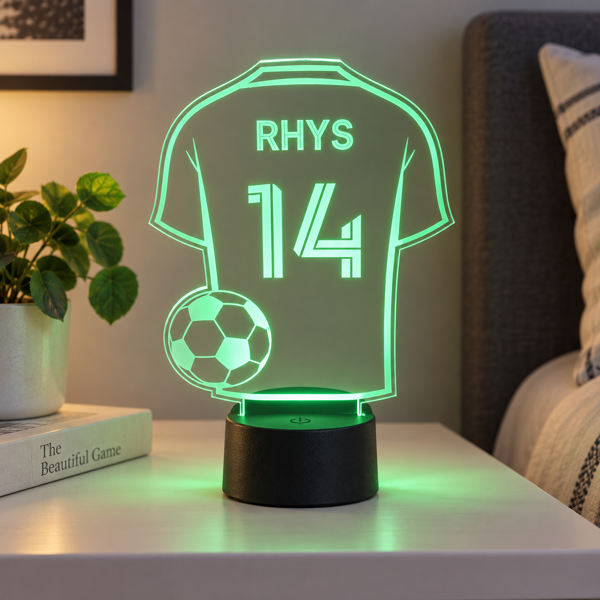 Football shirt night light personalised with Rhys 14, glowing green on a bedside table