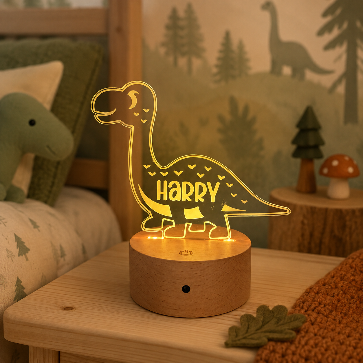 A glowing LED acrylic dinosaur night light shaped like a long-necked dinosaur, with the name 'HARRY' cut out in the center, sitting on a round wooden base on a child's bedroom bedside table.