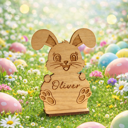 Wooden rabbit figurine with 'Oliver' on a grassy field with Easter eggs and flowers