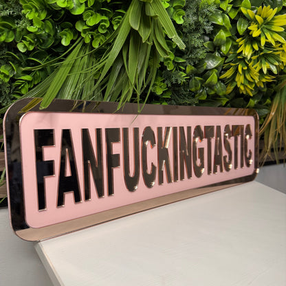 Metallic sign with text 'FANFECKINGTASTIC' on a white surface with green plants.