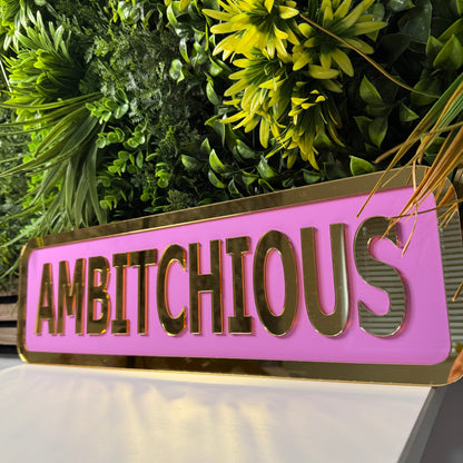 Pink and gold 'ABITICHOUS' sign with green foliage in the background