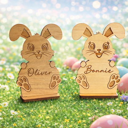 Two wooden rabbit figures named 'Oliver' and 'Bonnie' on a grassy background with Easter eggs.