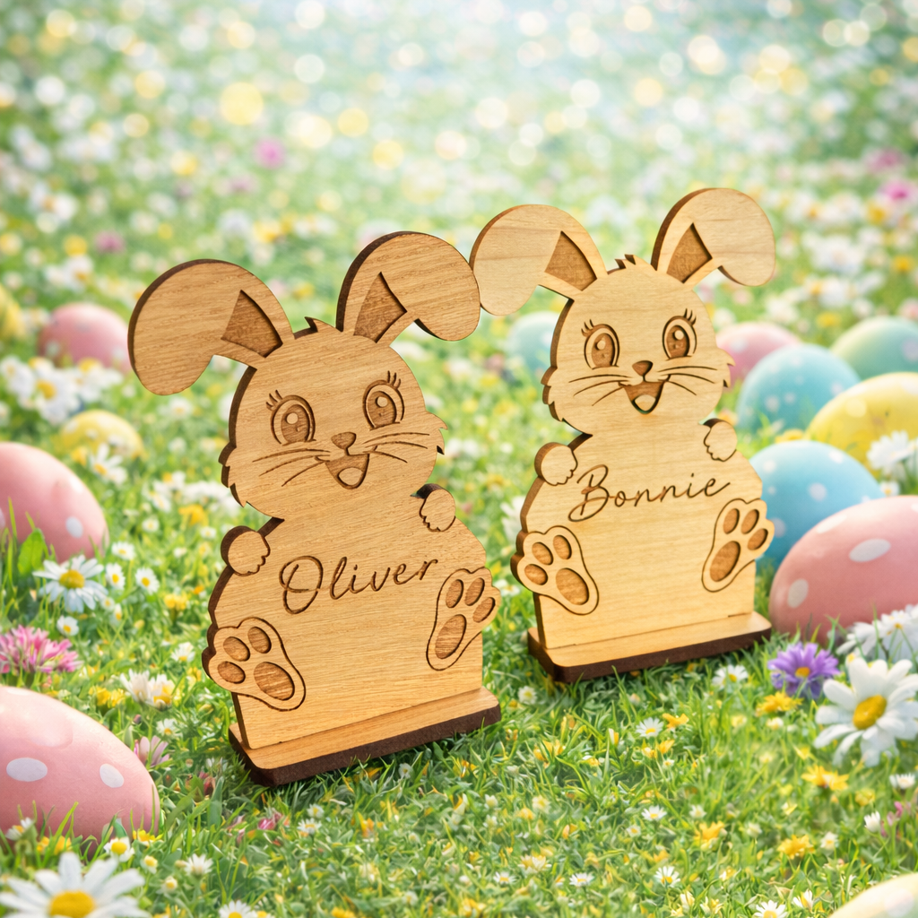 Two wooden rabbit figures named Oliver and Bonnie on a grassy field with Easter eggs and flowers.