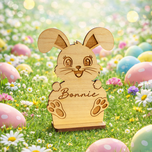 Wooden rabbit figurine with 'Bonnie' on a grassy background with Easter eggs and flowers