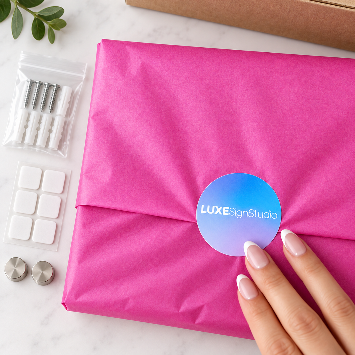 Order wrapped in pink tissue with a Luxe Sign Studio sticker, beside adhesive pads and wall fixings
