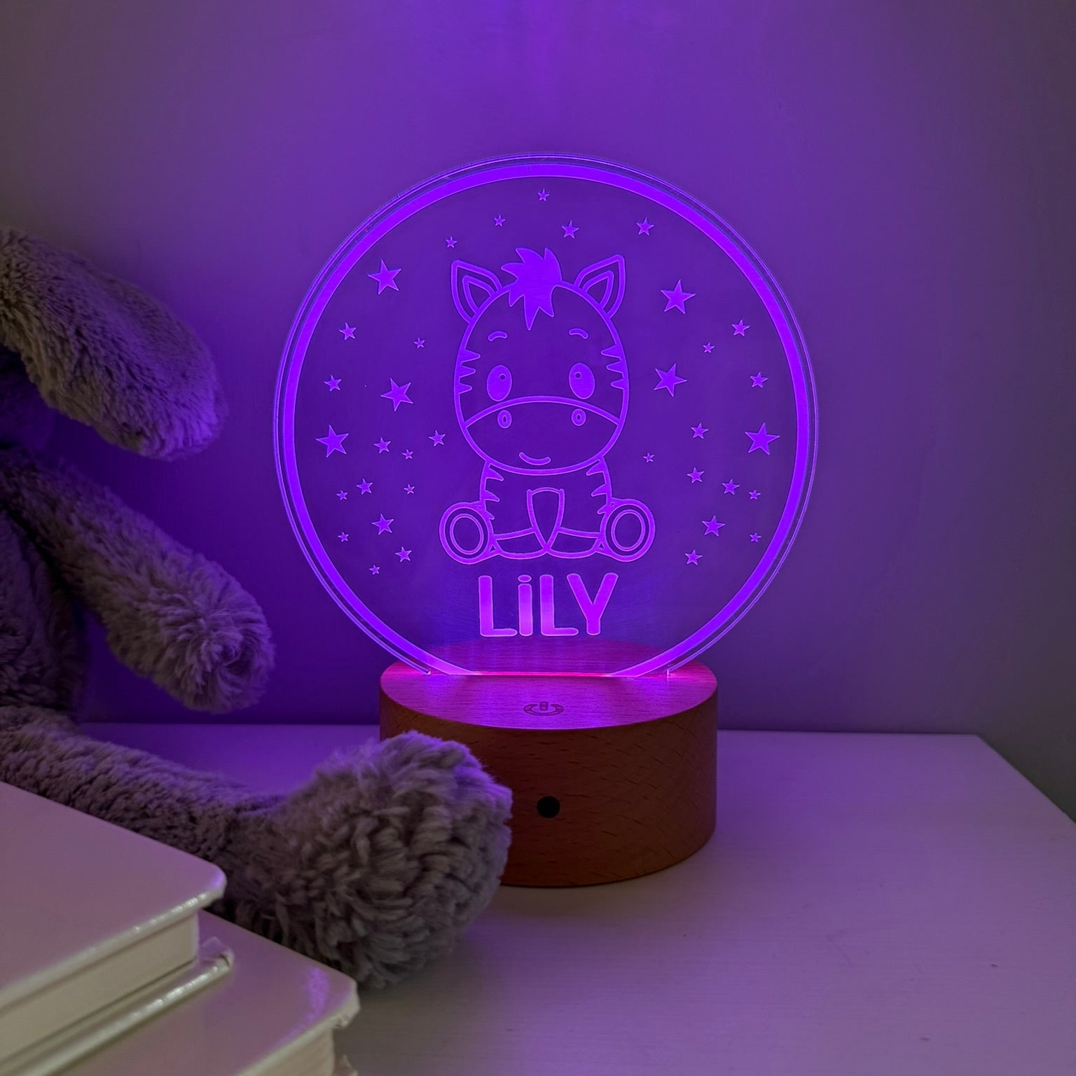 A personalized 3D optical illusion night light shaped like a round crystal ball, glowing with purple light. The design features a cartoon cat sitting on a bicycle with the name 'LILY' written below it, surrounded by stars.