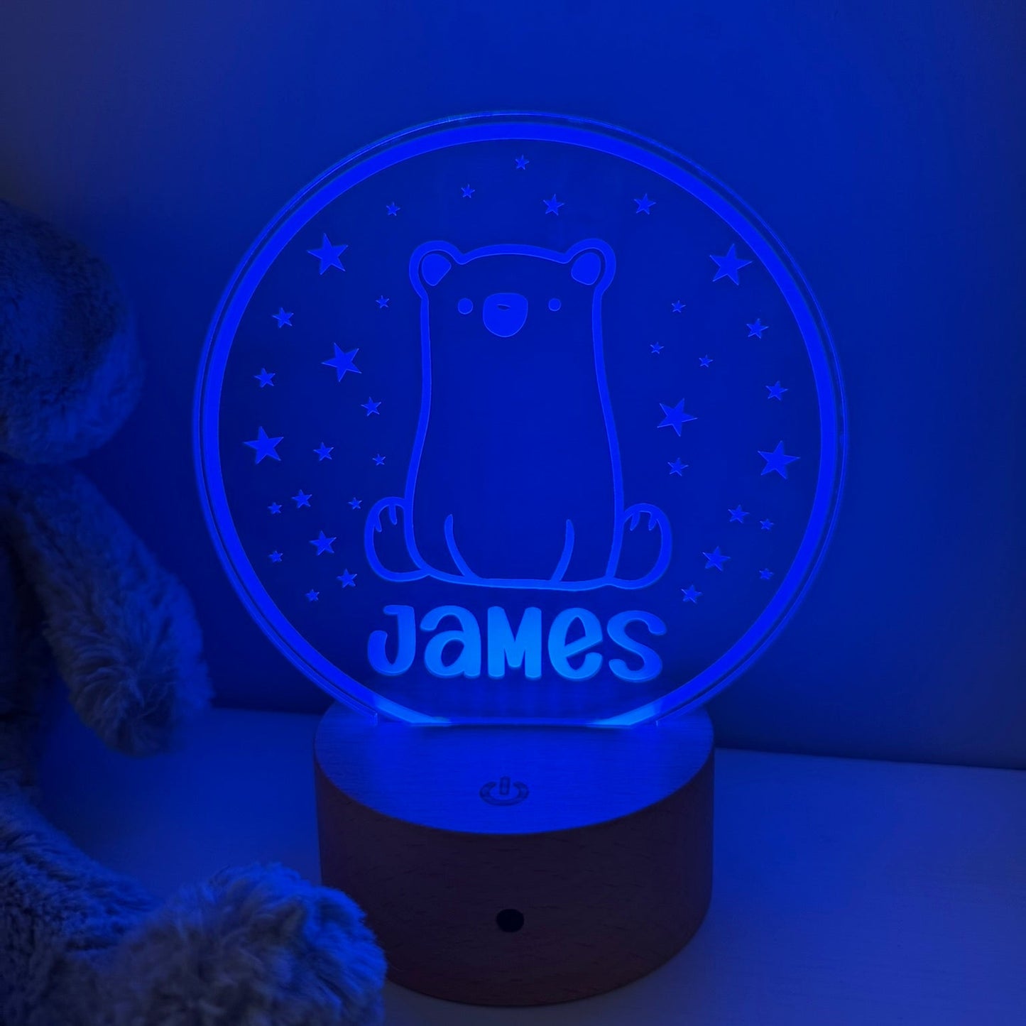 A personalized 3D optical illusion night light shaped like a bear sitting in a starry sky, glowing with a blue light. The name 'James' is custom printed at the bottom.