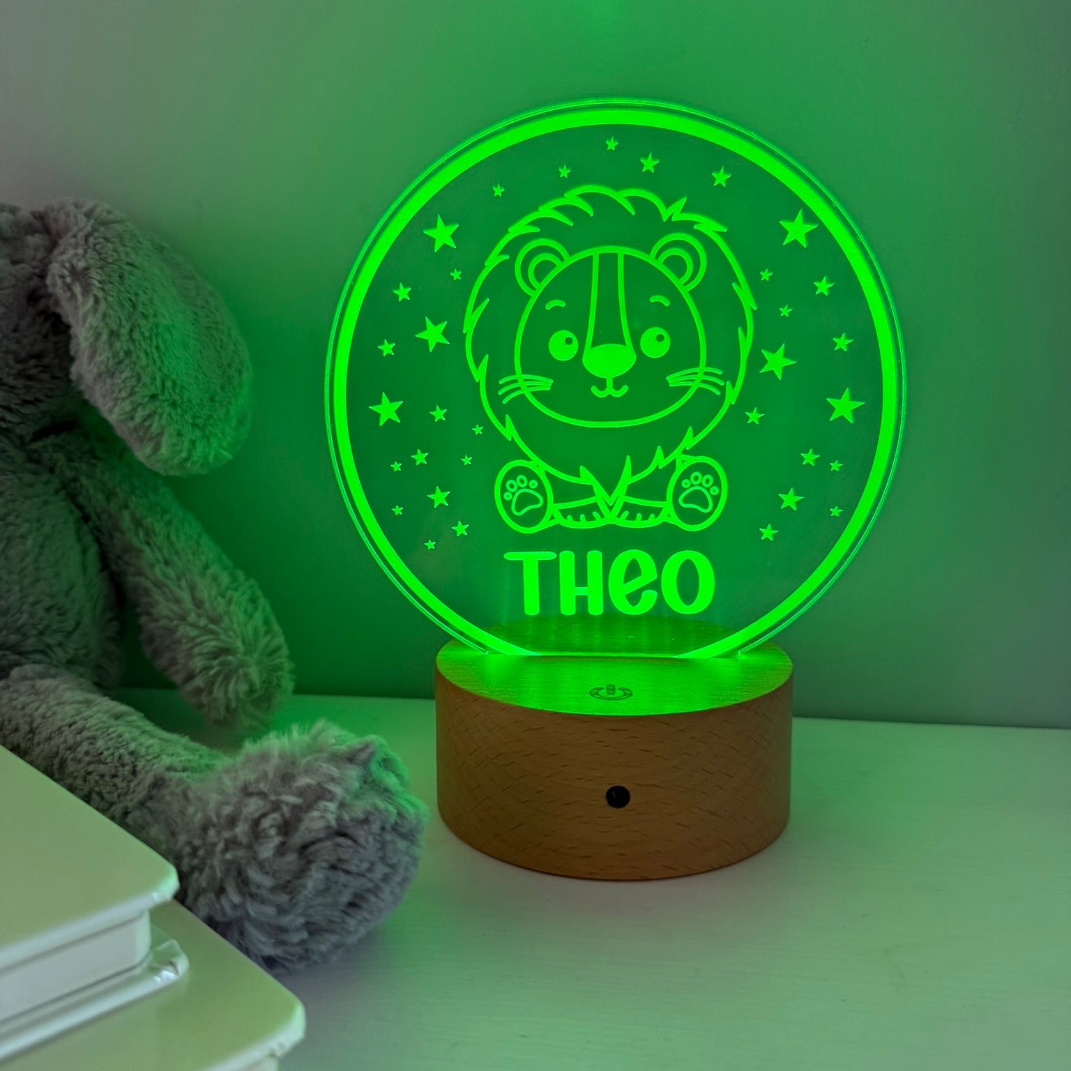 A personalized LED night light with a wooden base, featuring a glowing green circular panel with a lion illustration and the name 'THEO'.