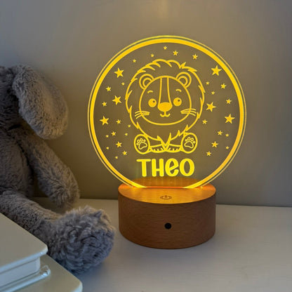 A personalized LED night light shaped like a glowing circular sign with a lion illustration and the name 'THEO', sitting on a wooden base on a tabletop next to a gray plush toy.