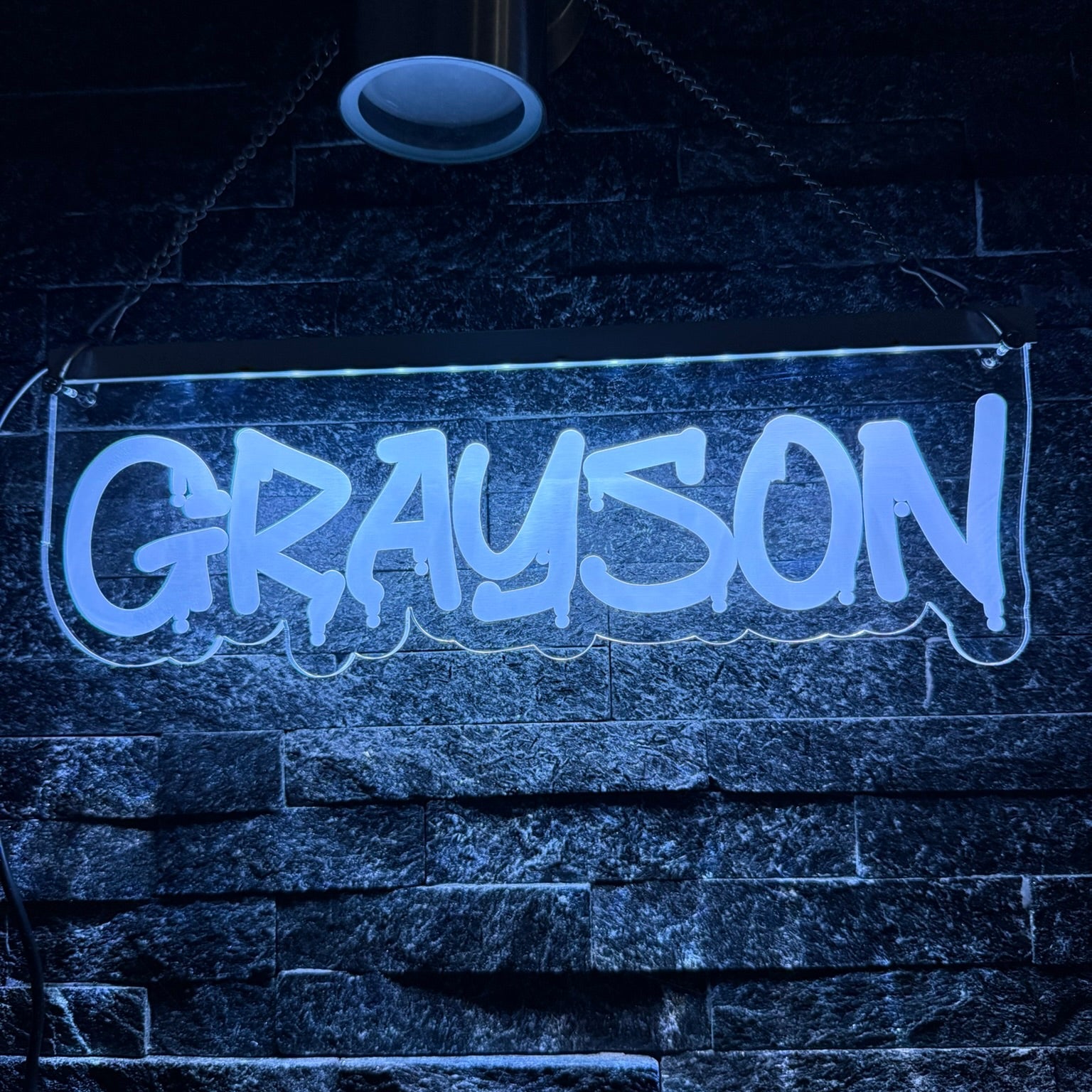 Neon sign with 'GRAYSON' on a dark stone wall