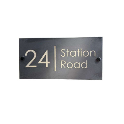 Rectangular black house number sign with '24 Station Road' text on a white background