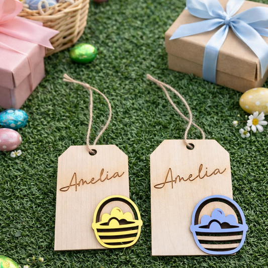 Two wooden tags with 'Amelia' engraved, each featuring a colorful easter egg design, on a grassy background with Easter eggs and gifts.